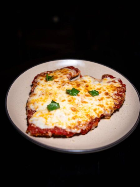 Breaded Chicken Parm cutlet topped with cherry tomato sauce, melted mozzarella, and fresh basil leaves.