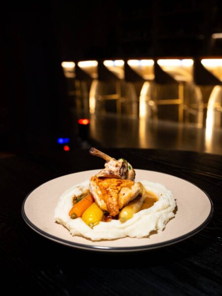 Pan-seared bone-in chicken breast resting on whipped mashed potatoes and roasted baby carrots with natural pan jus.