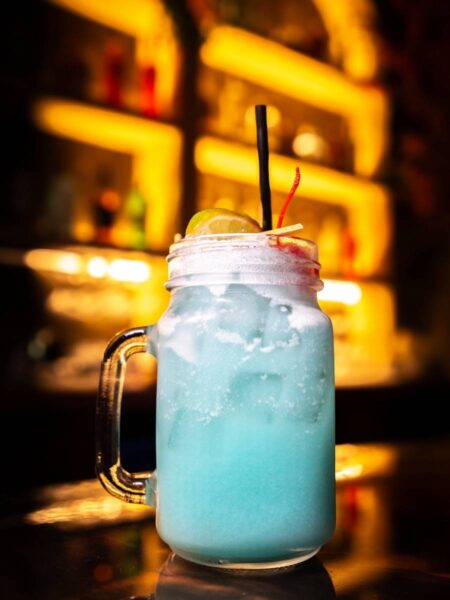 Vibrant blue Neon Coconut cocktail served in a glass mason jar mug garnished with a lime wheel and cherry.